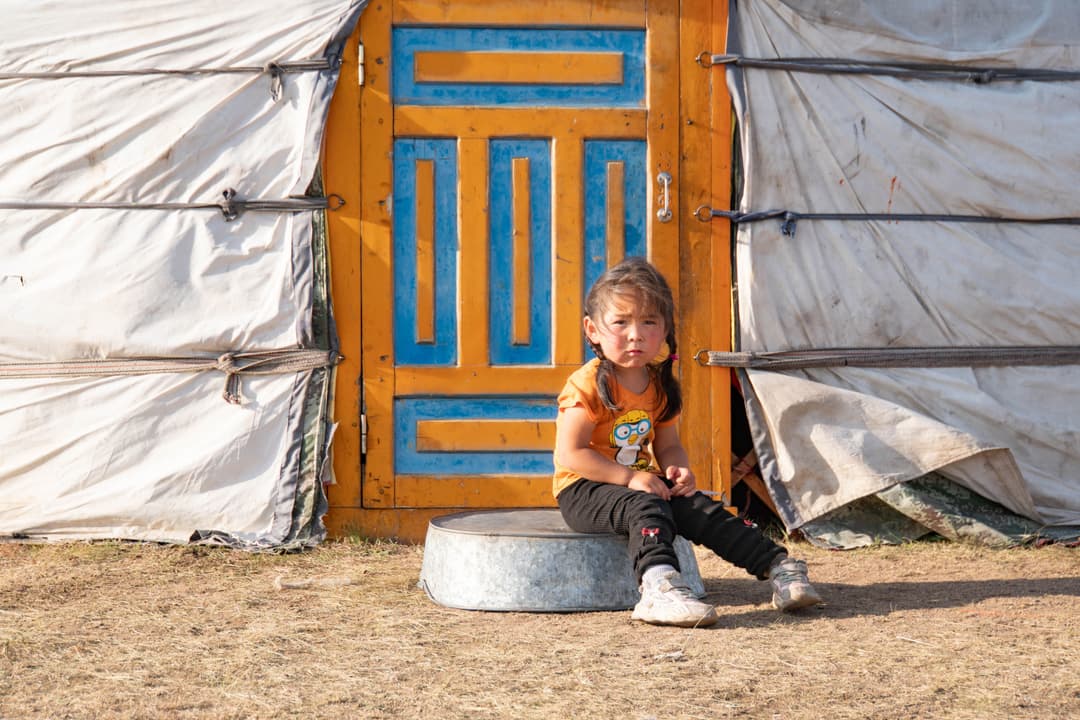 Young Mongolian girl sitting in front of her ger door