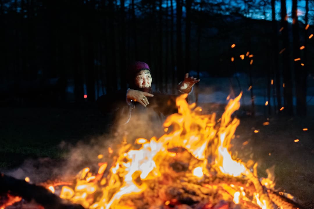 Elderly Mongolian Shaman woman during a fire ritual at night.